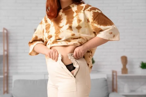 Image of woman trying to do her trousers up after pregnancy weight gain Blandford Camp